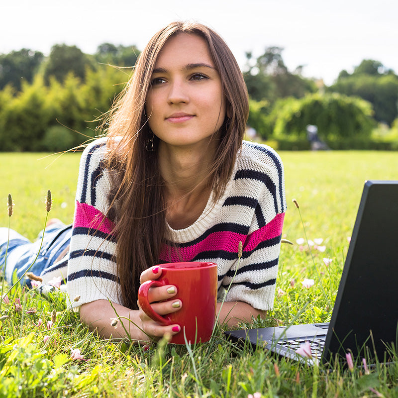 Girl holding CBD tea in red mug laying in the grass